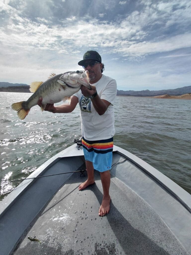 Fidel sosteniendo una lobina de 7.73 lb en lancha en Presa Bacurato durante un viaje de pesca en México.